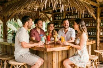 Groupe d'adultes dans un bar tropical tenant des cocktails colorés autour d'un comptoir en bois de palmier, ambiance détendue et conviviale